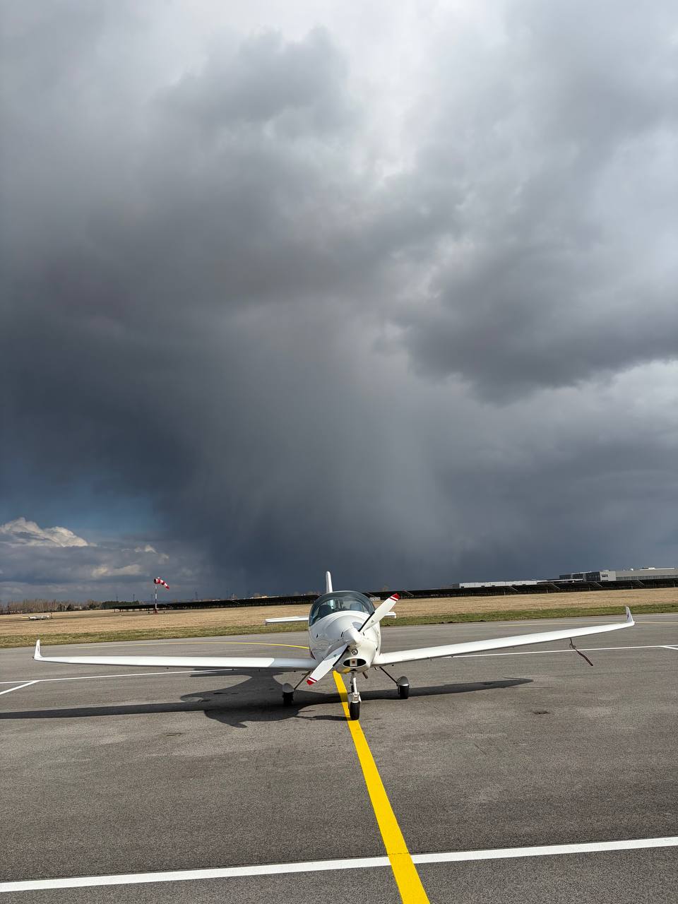 Small white single-engine aircraft on the apron under a heavy storm sky, rain shafts in the distance